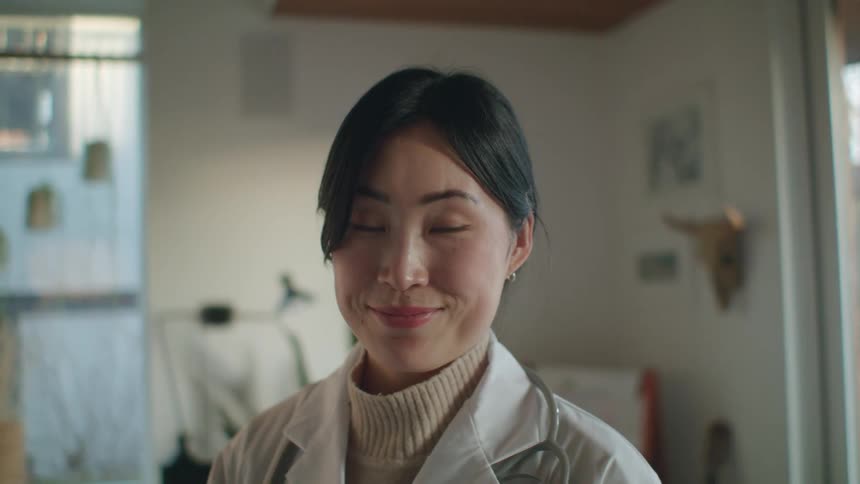 A doctor poses in her living room and takes off her blue surgical mask