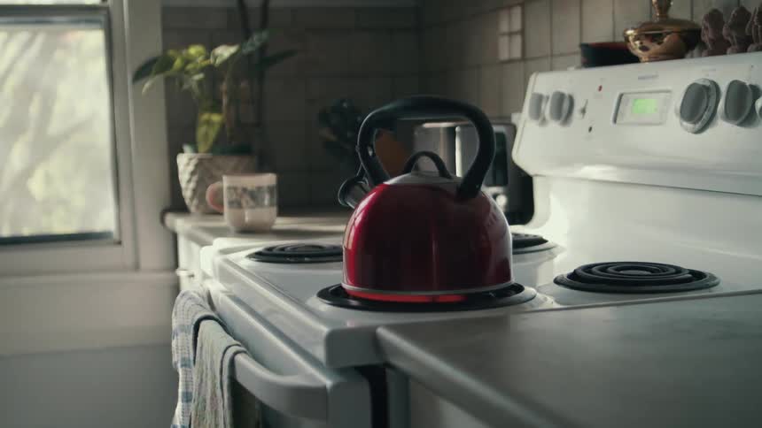A red tea kettle being heated on an electric stovetop in a home