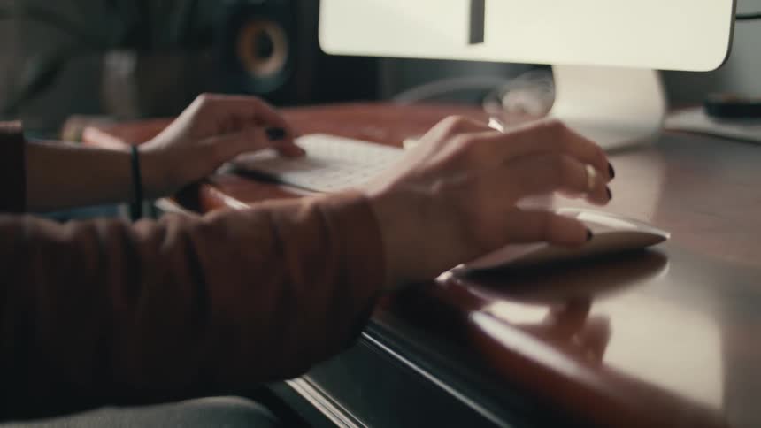 A woman sits at a desk with her hand on a computer mouse