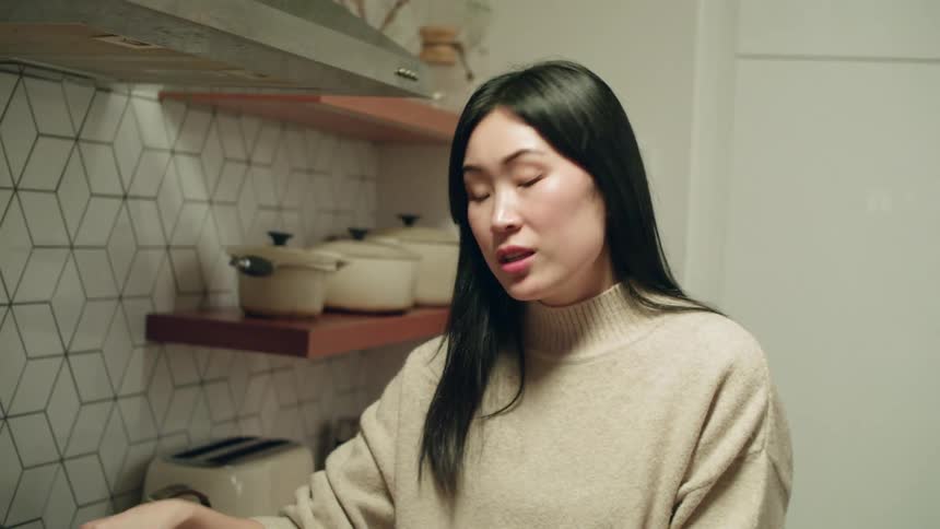 A woman talking while stirring a pan of food cooking on a gas stovetop