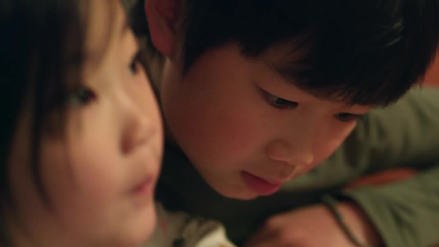 A boy and a girl laying on the floor looking at a tablet