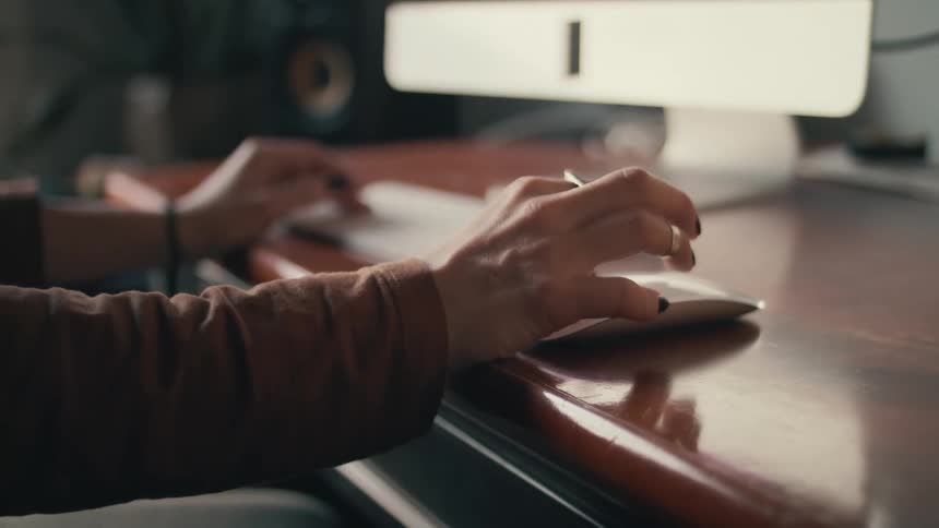 A woman with painted fingernails using a computer mouse at a desk