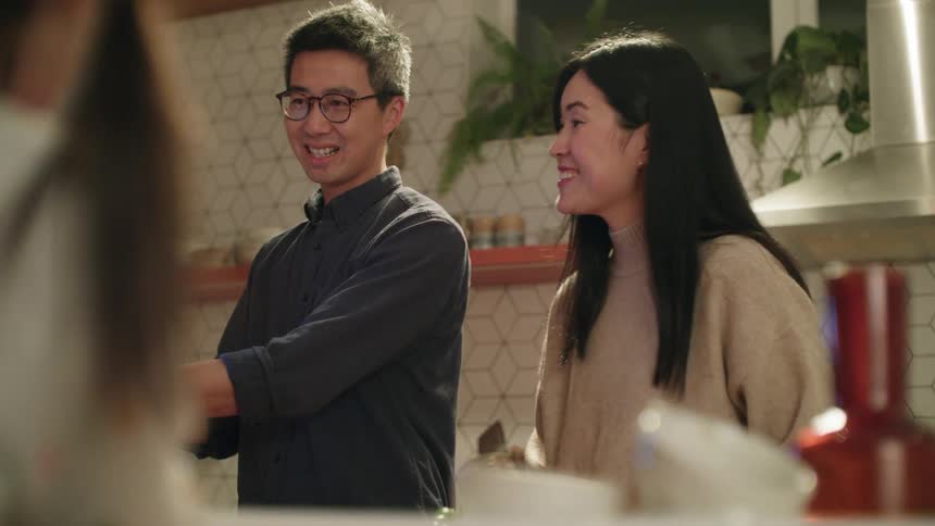 Mom and dad wave at someone on a tablet while their daughter sits in front of them in a kitchen