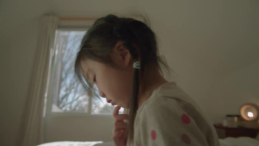 A little girls plays on a tablet while sitting on a bed during the day