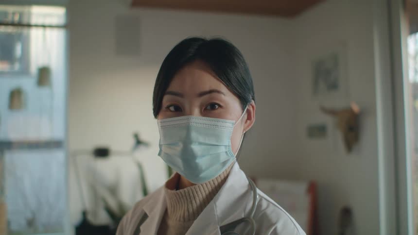 A female physician wearing a face mask and a white lab coat