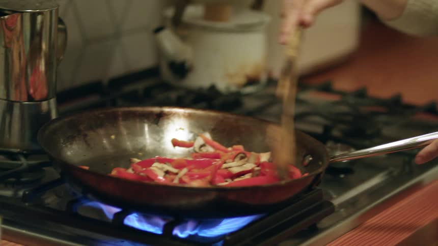 Happy young woman cooking dinner in a frying pan in the kitchen at home