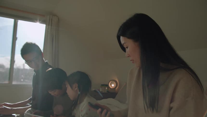 A mother answering a phone while sitting on a bed with her family