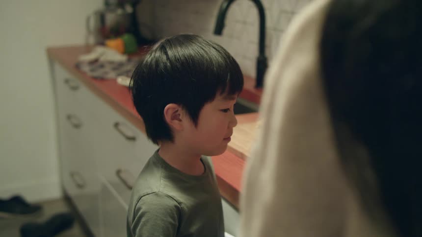 A mom cooks on a stove top while her son watches in a kitchen