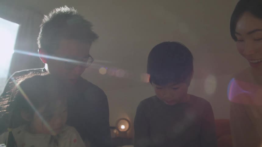 Parents helping their children with homework while sitting in a bed at home