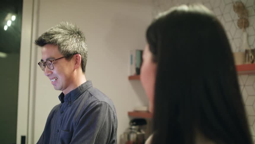 A man and woman laugh and talk as the woman chops vegetables at home