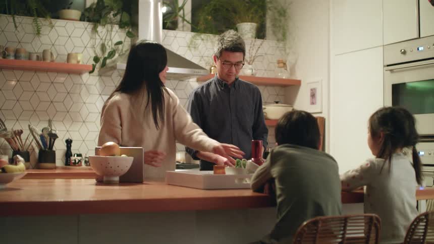 A little boy and girl sit at a kitchen island as their mom and dad prepare a meal