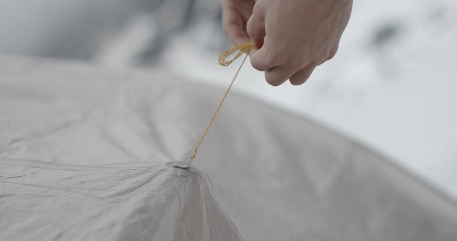 A man's hands work a string on what looks like tent fabric