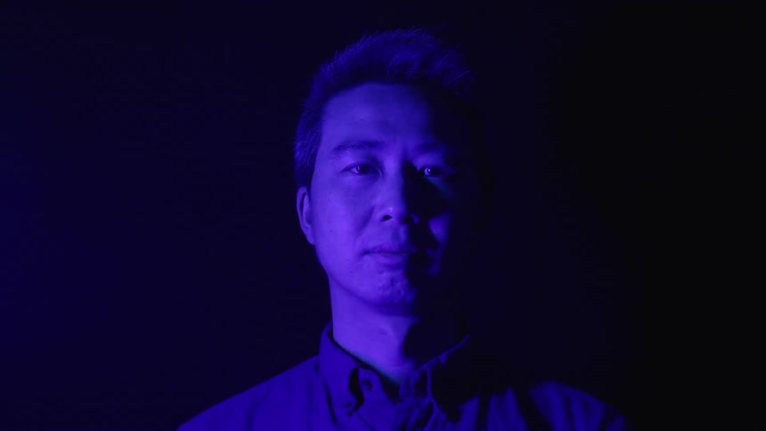 Color changing lights flash across the face of a man who smiles while standing against a wall