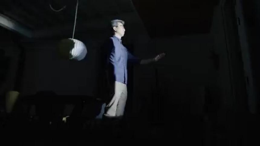 A man walks through his living room and slowing reaches his arm out as lights flash on and off