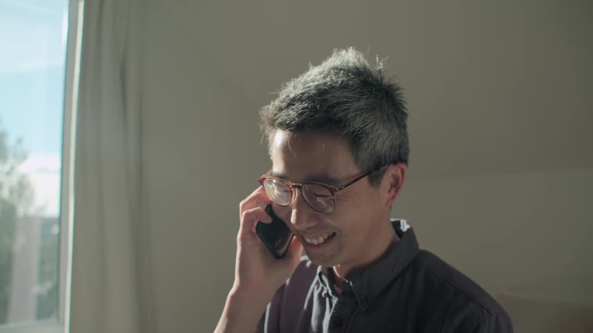 A man in a room talking on a phone and smiling
