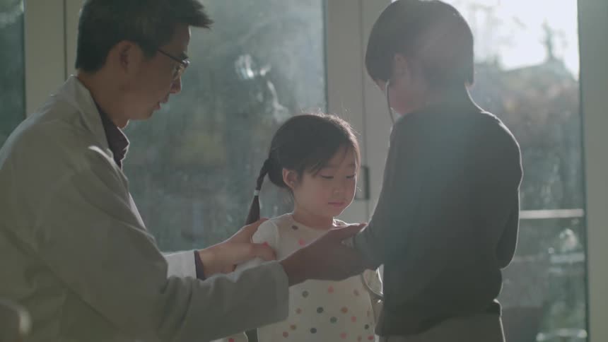 A doctor making a house call lets two young children use his stethoscope