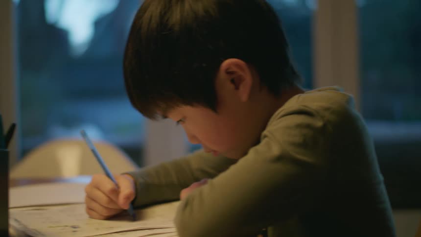 A little boy sits at home and does school work