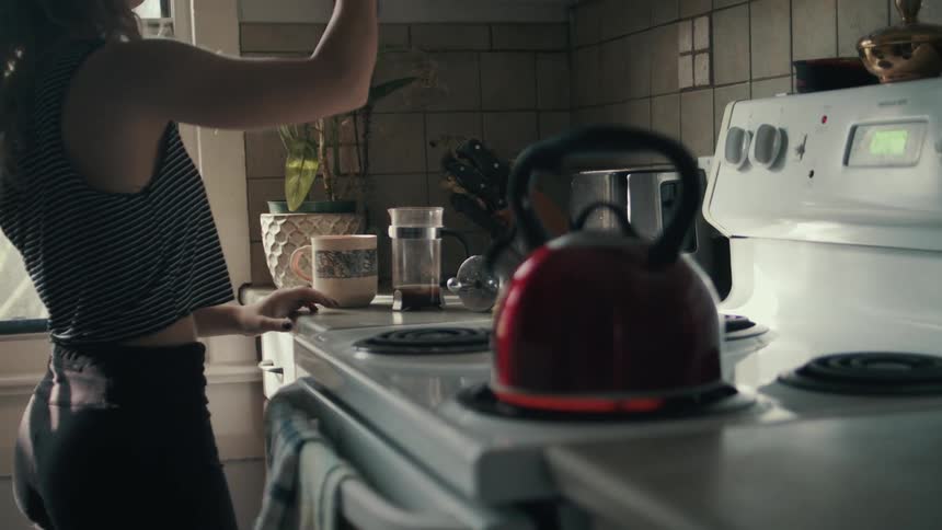 A young woman drinking coffee opens a cupboard in the kitchen in the morning