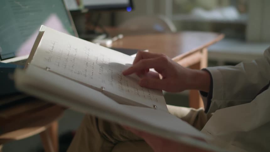 A doctor in a white lab coat reading through notes at a desk