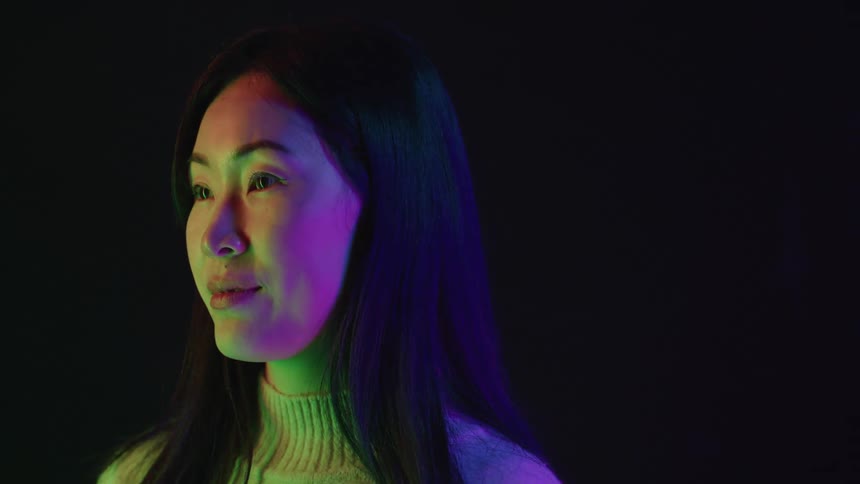 A woman standing in a room with multicolored lights shining on her face