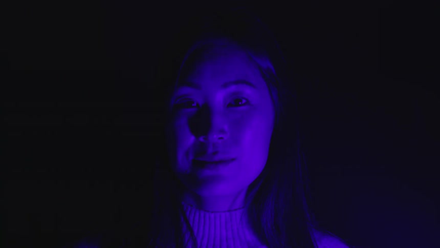 A young woman in a blue light with shadows casting on her