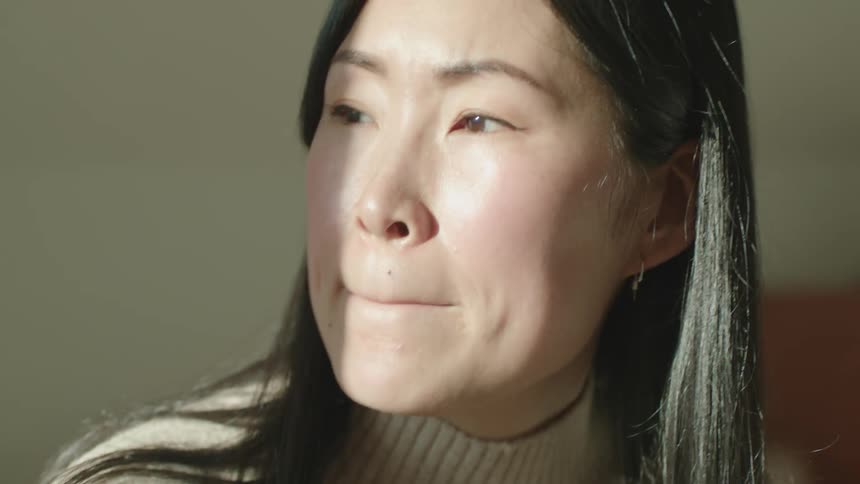 An asian woman smiling and shaking her head while in thought