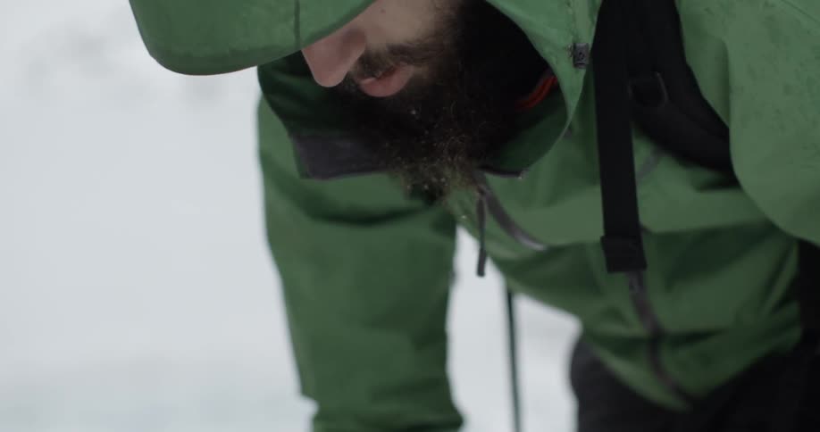 A man bending over and looking at something in the snow