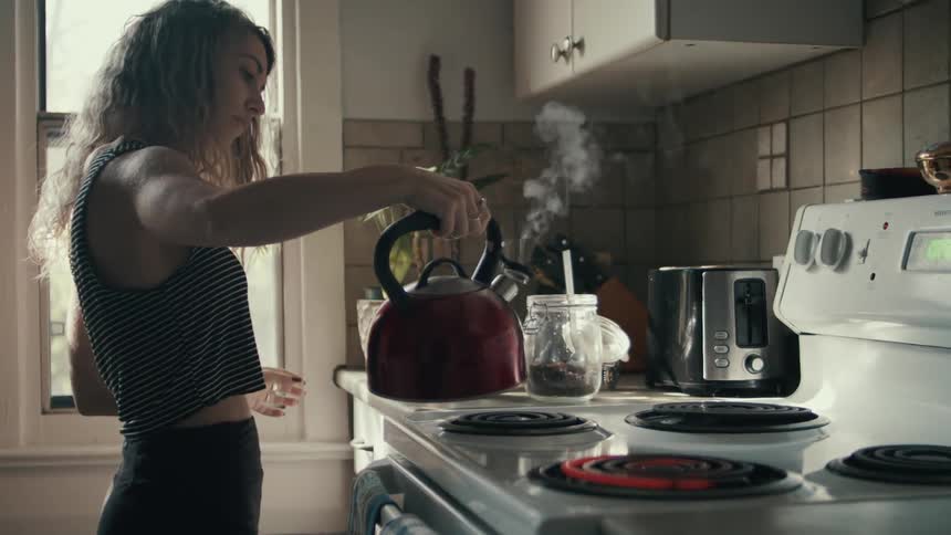 Young woman making coffee boils water in a kettle in the kitchen at home
