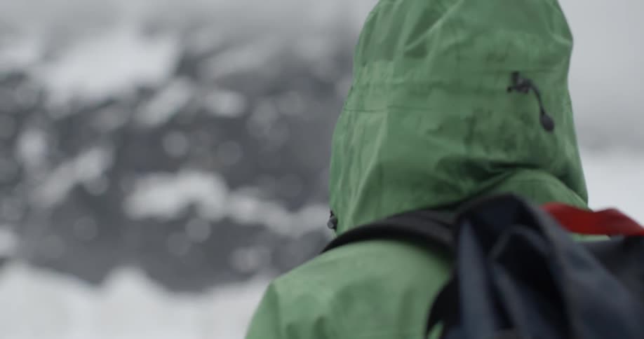 A person is standing with hood up looking at a mountain