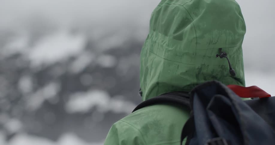 A man in a winter coat stands and looks up at a snow-covered hillside