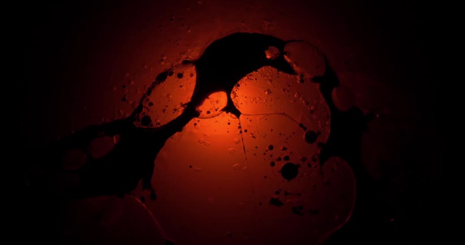 Black liquid ink floating on the surface of a clear liquid over a red light
