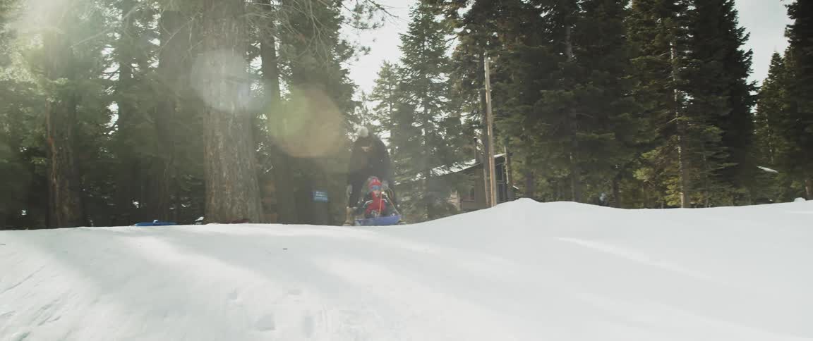 Mother and son sitting on a sled getting ready to go down a snow covered slope