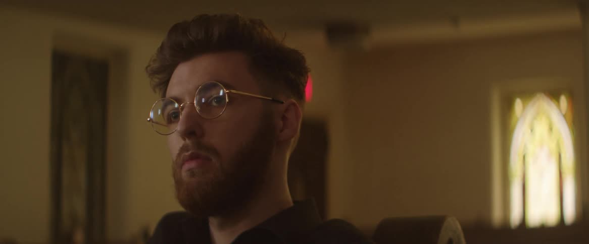 Young bearded man wearing glasses sitting in a pew at church attending mass
