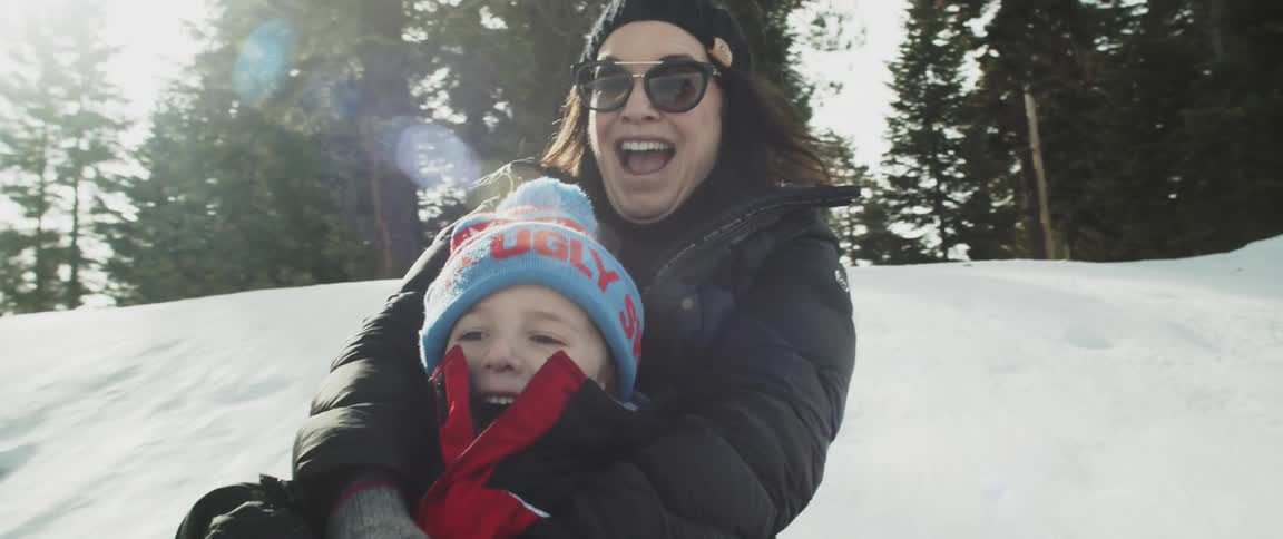 Mother and son sliding in the snow of a small slope on a sled in the morning