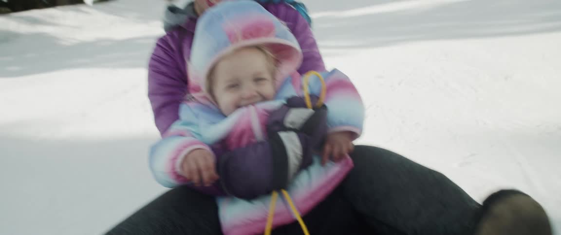 A mother and daughter sliding on a sled on snow with trees the sky and clouds in the background