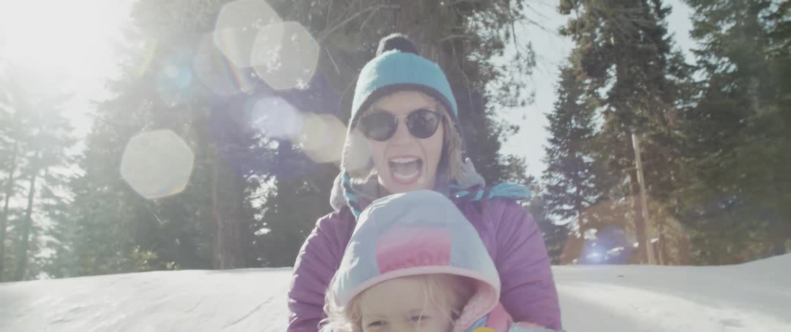 A woman and child riding a sled down a snowy hill