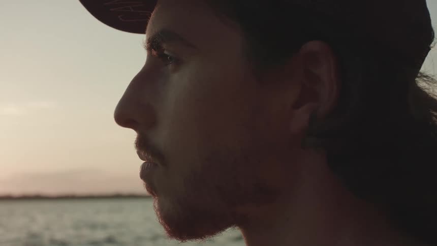 A man stands outdoors and stares ahead while he is near coastal waters