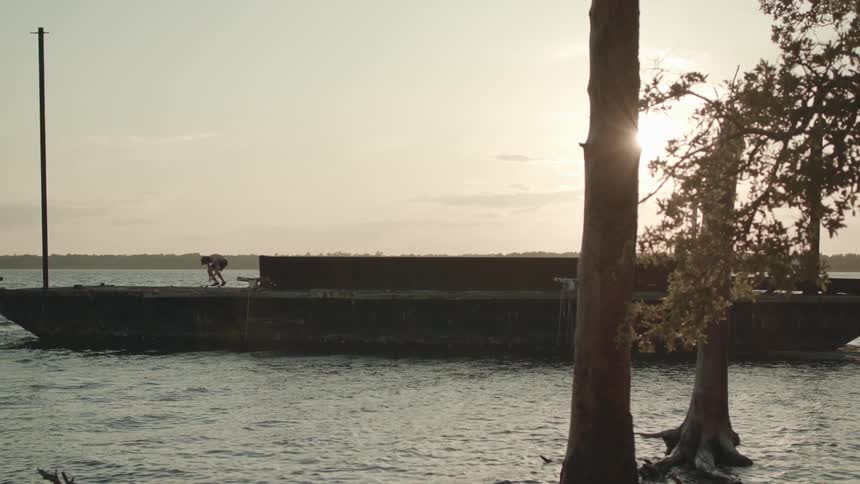 A man performs a kick flip of his skateboard close to the edge of the water