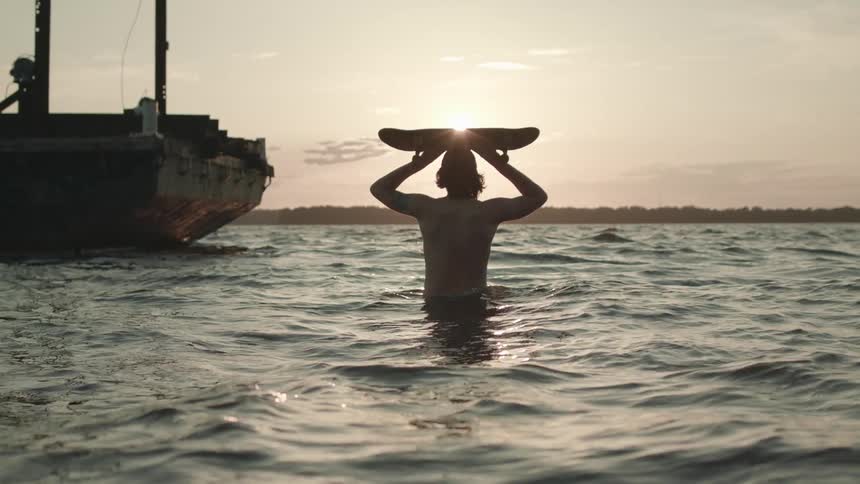 A man carries a board into the water