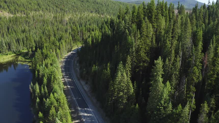 A two lane highway winds through a forest near a lake