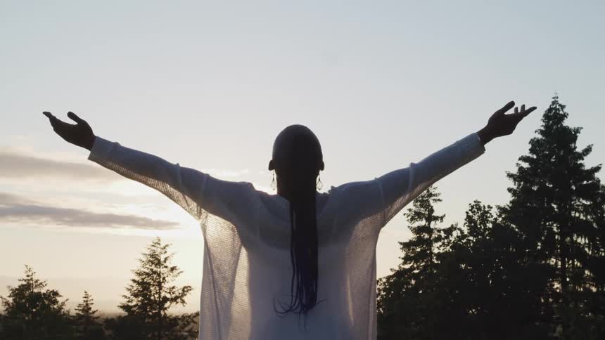 A woman raises her hands above her head as she stretches outside