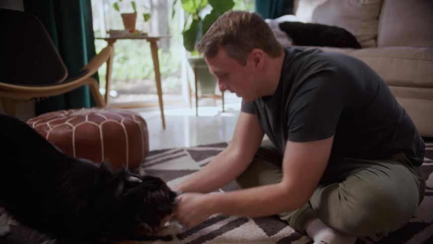 A man sitting indoors plays fetch with his excited pet dog