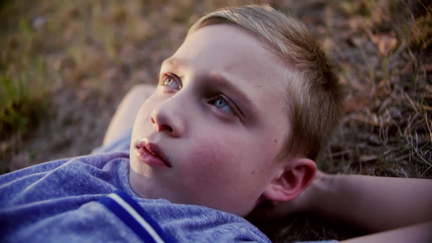A young boy lies on grass with his hands behind his head