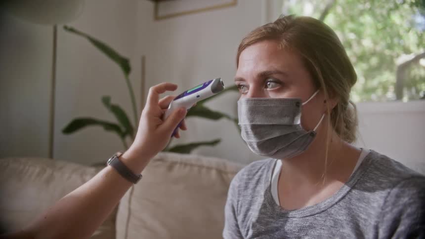 A nurse takes a womans temperature at her home