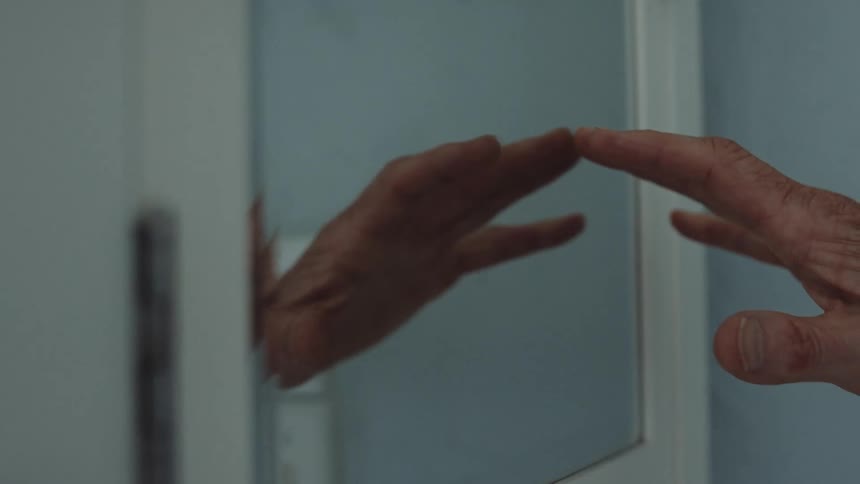 A man reaches out his hand to touch his bathroom mirror