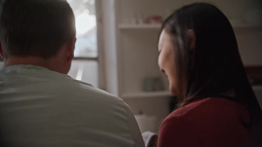 A man and a woman in a kitchen talking and smiling with a window in the background