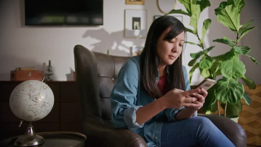 A teenage girl sits at home and scrolls on her cellphone