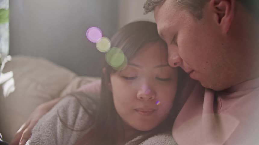 A man holds and rubs his wifes hand as they cuddle on the couch at home