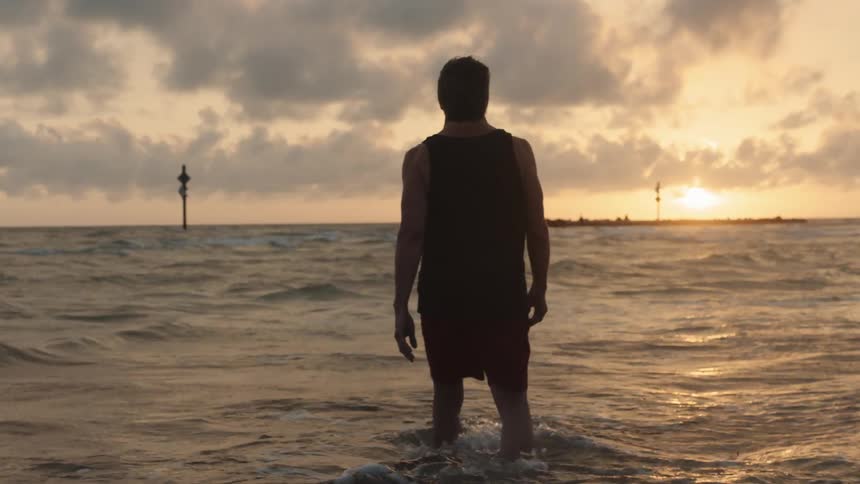 A man walking in to the ocean as the sun sets