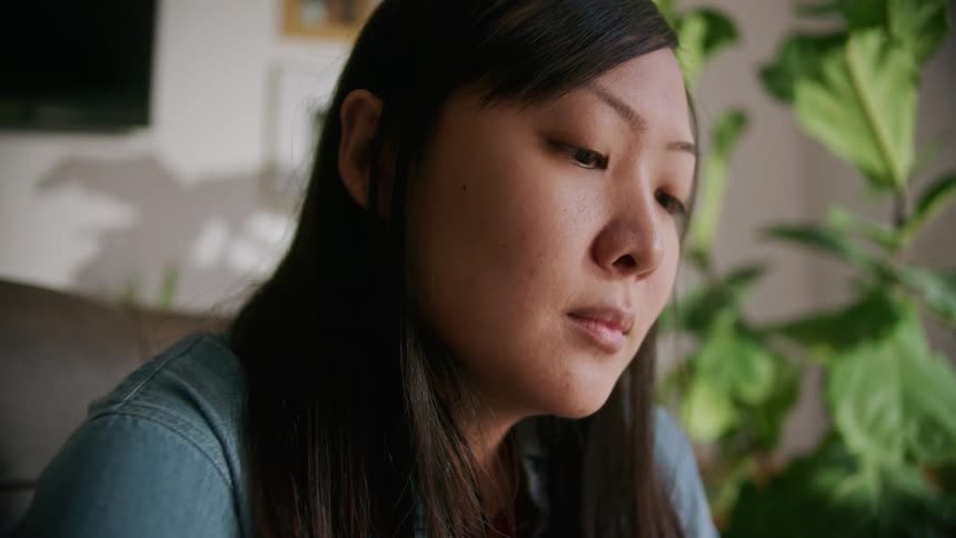 An asian woman sits indoors while looking down as she concentrates on what she is reading